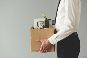 Getting fired. Cropped image of handsome businessman in formal wear holding a box with his stuff, on gray background